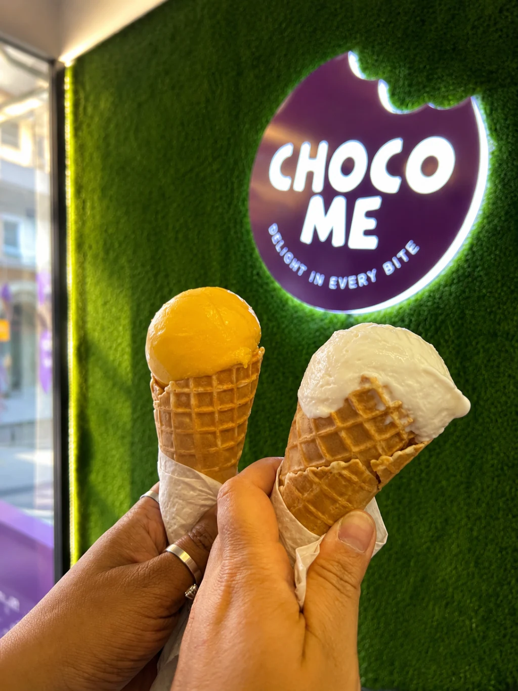A photo-friendly feature wall designed to encourage customer engagement, social sharing, and organic brand visibility. Customers holding ice cream cones in front of the illuminated Choco Me feature wall, creating a shareable branded photo moment.