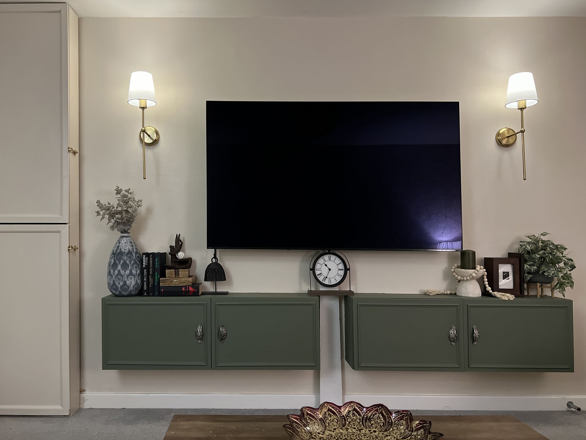 Custom sage green floating TV console with brass wall sconces in a modern luxury living room designed by House of Ahana in Yorkshire.